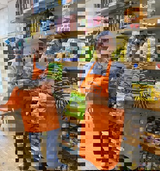 two women in orange aprons in front of pantry food smiling