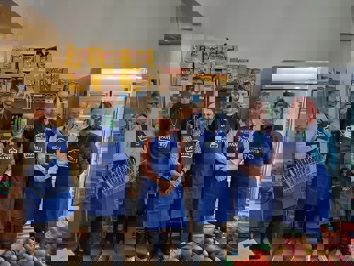 6 people in blue pantry aprons in front of apples and other various food