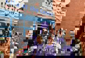 pantry volunteers in purple aprons in front of pantry shop front with a man holding a shopping basket