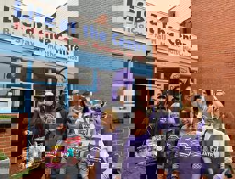 pantry volunteers in purple aprons in front of pantry shop front with a man holding a shopping basket
