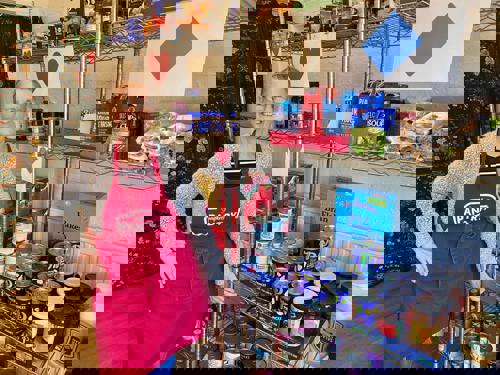 A smiling lady in a Pantry apron stands by canned food on shelves