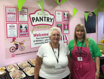 two woman one in a red apron in front of Whitby pantry sign