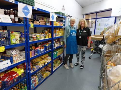 Two ladies standing by blue shelving with packet food and food in cans