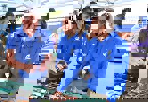 two woman in blue jumpers speaking with a man in a blue shirt 