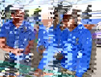 two woman in blue jumpers speaking with a man in a blue shirt 