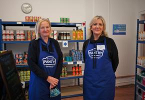 two woman in blue aprons inside a food pantry