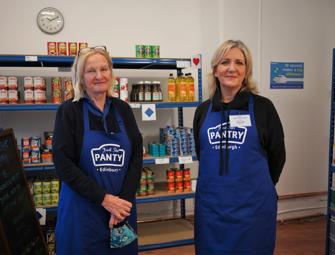 two woman in blue aprons inside a food pantry