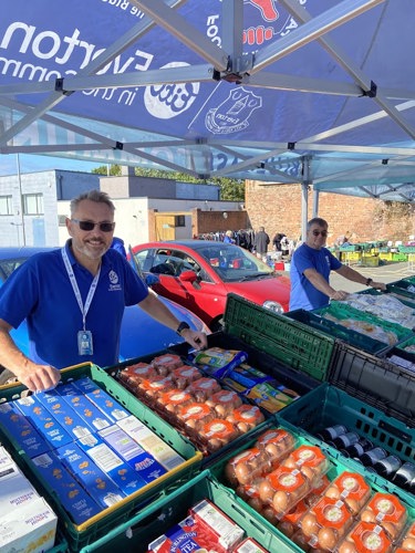 Two men under a pop up tent with food in crates