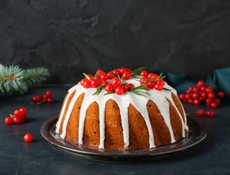 close up of Christmas Cake on a black table topped with red berries