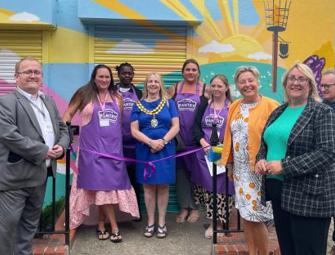 mayor and pantry volunteers in purple aprons next to a ribbon for opening event