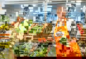 woman in orange apron holding tomatoes and broccoli 