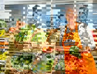woman in orange apron holding tomatoes and broccoli 