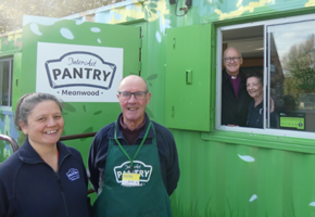 bishop and woman in front of green shed with pantry logo