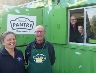 bishop and woman in front of green shed with pantry logo
