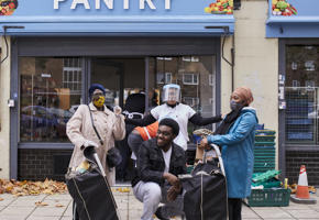 happy people in masks in front of blue pantry sign 