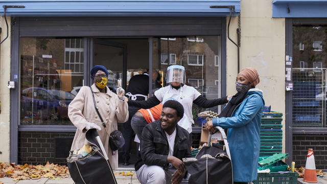 happy people in masks in front of blue pantry sign 