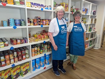 two women in blue aprons against food on shelves 