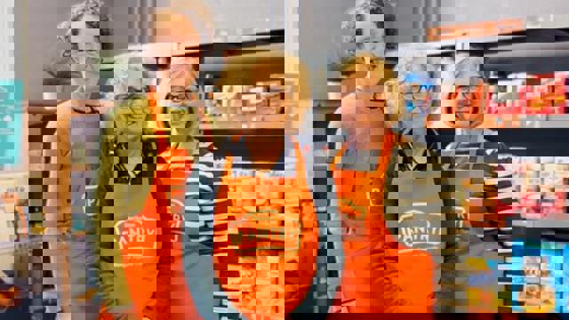 3 woman in orange aprons in front of food shelves 