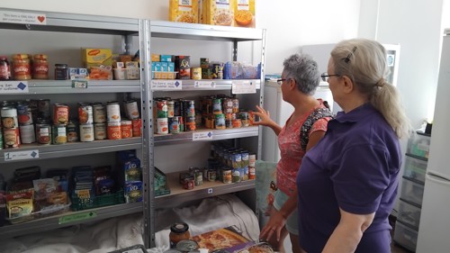 Two ladies browse a shelf of canned food