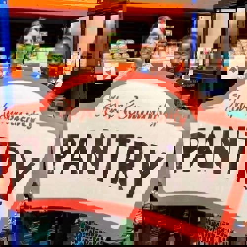 Two smiling ladies holding a large Hope Community Pantry logo