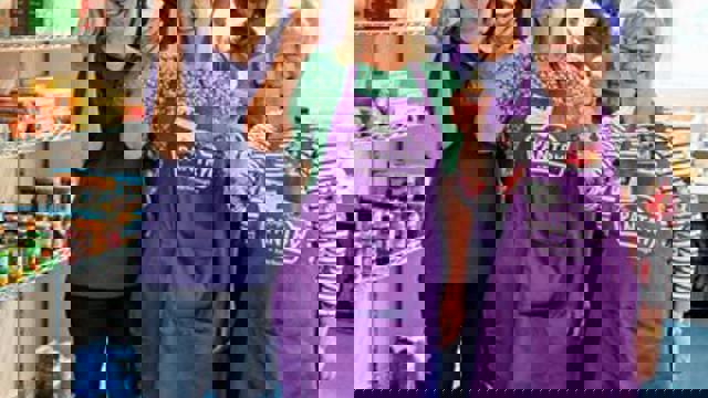 group in purple aprons holding up cupcakes