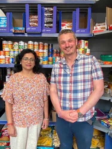 A man and a lady standing behind shelves of canned food