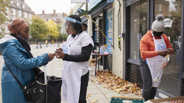 woman in front of pantry with plastic mask showing another woman a phone