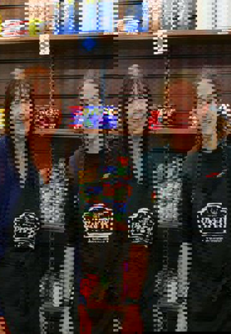 two woman in black aprons in front of food shelves 