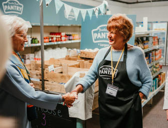 Woman holding a hand of another woman within a pantry