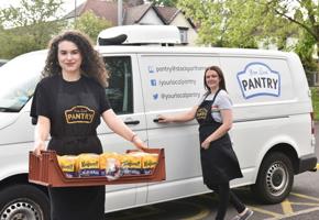 two woman outside of a your local pantry van with one holding a food tray with bread